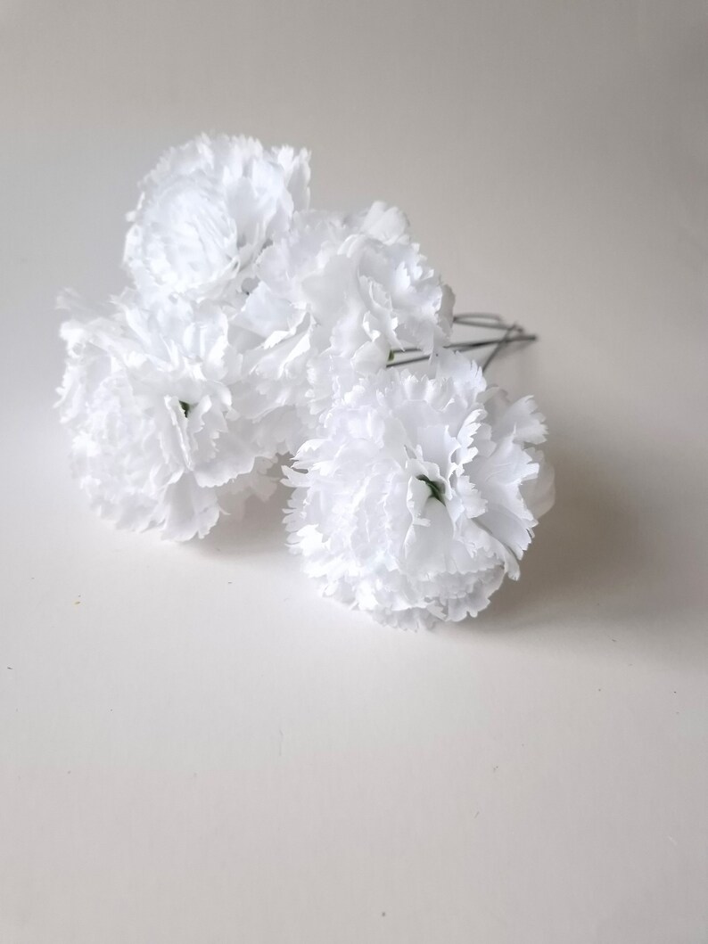May include: A bunch of white carnations with green stems, arranged in a cluster. The carnations are artificial and have a realistic appearance.