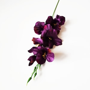 Puede incluir: Un solo tallo de flores de gladiolo artificiales de color púrpura con hojas verdes.