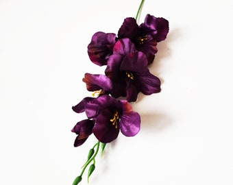May include: A single stem of artificial purple gladiolus flowers with green leaves.