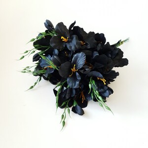 May include: A bouquet of black silk flowers with yellow centers and green stems. The flowers are arranged in a cluster and are facing towards the camera.