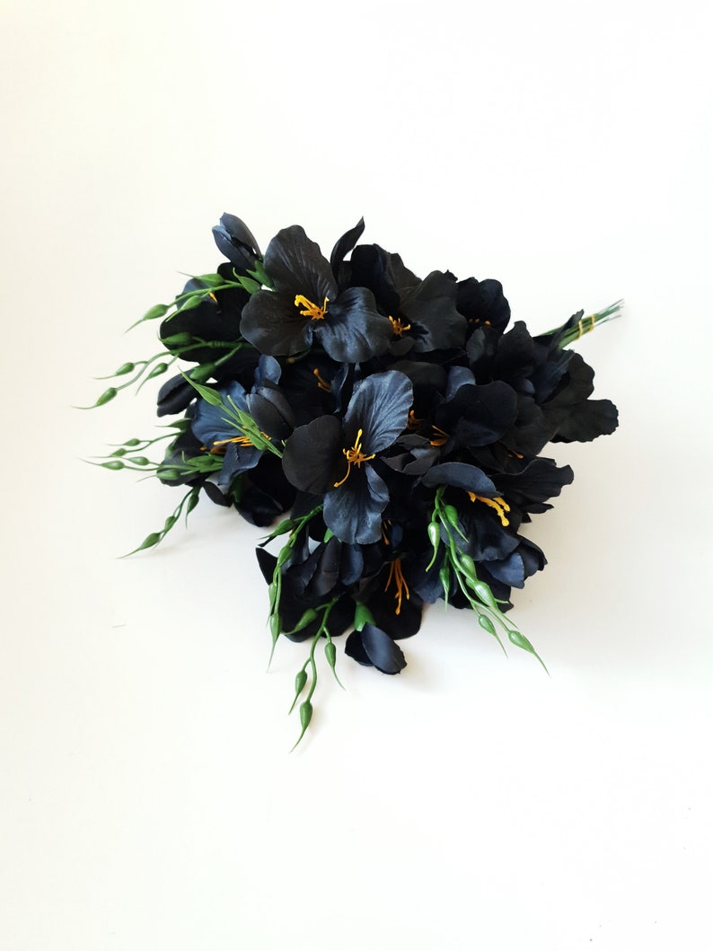 May include: A bouquet of black silk flowers with yellow centers and green stems. The flowers are arranged in a cluster and are facing towards the camera.