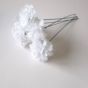 May include: A bunch of white carnations with green stems attached to thin black wires. The carnations are arranged in a cluster.