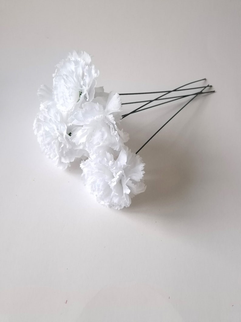 May include: A bunch of white carnations with green stems attached to thin black wires. The carnations are arranged in a cluster.