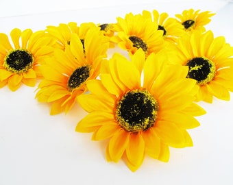 May include: A cluster of yellow artificial sunflowers with black centers. The sunflowers are arranged in a circular pattern on a white background.