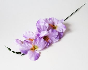 May include: A bouquet of artificial purple flowers with green stems. The flowers have a delicate, ruffled appearance.