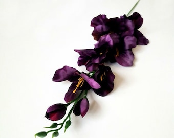 May include: A single stem of purple artificial flowers with green leaves and buds.
