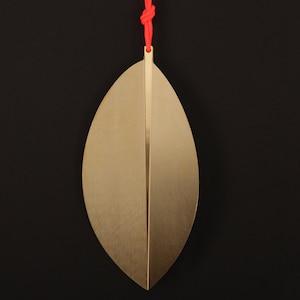 May include: A gold leaf-shaped bookmark with a red string attached to the top.