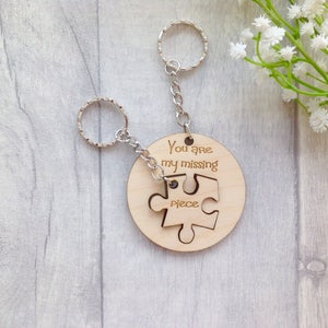 May include: A wooden keychain with a jigsaw piece design. The keychain has a silver chain and two key rings. The wooden piece says "You are my missing piece".