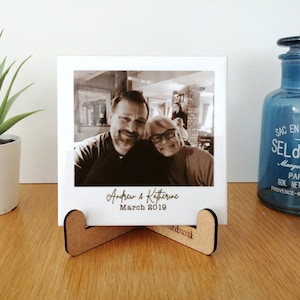 May include: A black and white photograph of a couple, Andrew & Katherine, on a ceramic tile with a wooden stand. The photo was taken in March 2019.