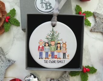 Puede incluir: Un adorno navideño de cerámica blanca con una familia de seis personas de pie frente a un árbol de Navidad decorado. La familia lleva ropa festiva y el adorno incluye el texto "The O'Kane Family".