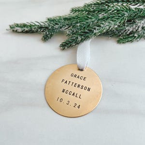 以下が含まれることがあります： 「GRACE PATTERSON MCCALL 10.3.24」と刻まれた丸い金色のオーナメント