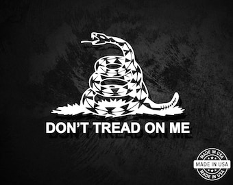 May include: A black and white image of a coiled rattlesnake with the words "Don't Tread On Me" below it. The snake is a symbol of the American Revolution and is often used as a political statement. The image is made in the USA.