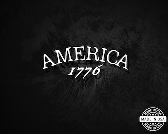 May include: A black background with the word "AMERICA" in white, arched above the number "1776". A small "Made in USA" emblem is in the lower right corner.