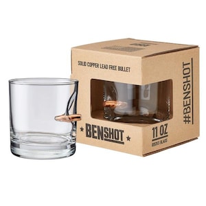 Puede incluir: Dos vasos de rocas de vidrio transparente con una bala de cobre incrustada en el lateral. Los vasos est&aacute;n empaquetados en una caja de cart&oacute;n marr&oacute;n con el texto "Benshot" y "Solid Copper Lead Free Bullet" impreso en la caja. La caja tambi&eacute;n tiene el texto "#Benshot" y "11 oz Rocks Glass".