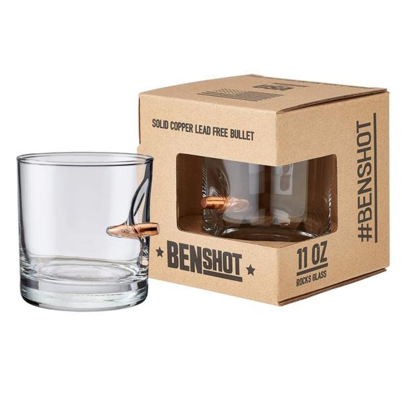 Puede incluir: Dos vasos de rocas de vidrio transparente con una bala de cobre incrustada en el lateral. Los vasos est&aacute;n empaquetados en una caja de cart&oacute;n marr&oacute;n con el texto "Benshot" y "Solid Copper Lead Free Bullet" impreso en la caja. La caja tambi&eacute;n tiene el texto "#Benshot" y "11 oz Rocks Glass".