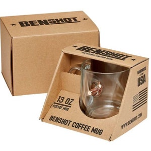 May include: A brown cardboard box with the text "BENSHOT" printed on the top. The box contains a clear glass coffee mug with a bullet-shaped handle. The mug is labelled "13 oz Coffee Mug" and "BENSHOT COFFEE MUG". The box also has the text "Handmade in the USA" and "www.benshot.com" printed on it.