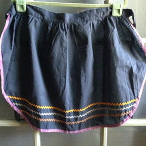 May include: A dark blue apron with a pink, orange, and gray zig-zag trim around the bottom.