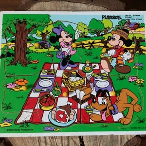 以下が含まれることがあります： ミッキーマウス、ミニーマウス、プルートがピクニックをしている木製パズル。パズルは6ピースで、アメリカ製。1歳半から4歳のお子様向けです。