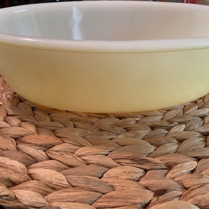 May include: A large, oval-shaped, yellow ceramic baking dish. The dish is sitting on a woven brown mat.