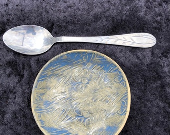 May include: A blue and yellow ceramic bowl with a textured design. A silver spoon is placed next to the bowl.
