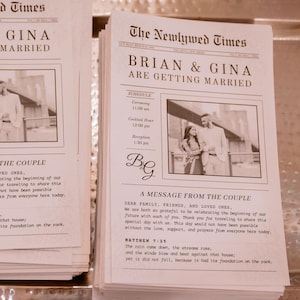 May include: A stack of wedding announcement cards with the headline "The Newlywed Times." The cards feature the names "Brian & Gina" and include a schedule, a message from the couple, and a Bible verse.