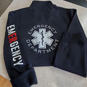 May include: Black zippered jacket with a white star of life logo and the text "Emergency Department" on the back. The left sleeve has the word "Emergency" printed vertically in red and white.