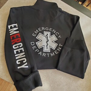 May include: Black zippered jacket with white text on the sleeves that reads "EMERGENCY" and a white star of life logo on the back with the text "EMERGENCY DEPARTMENT".