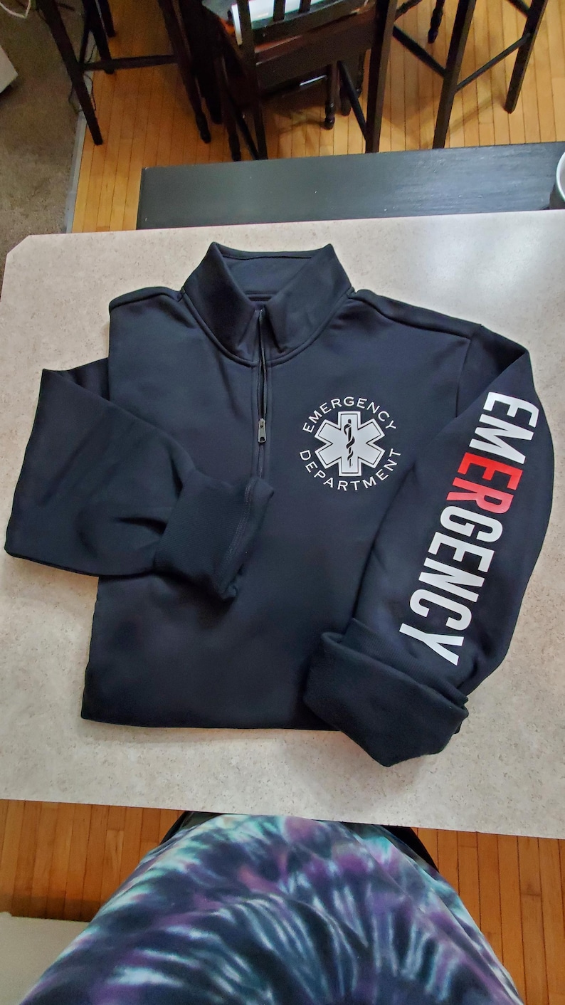May include: Black zippered sweatshirt with a white star of life logo and the text "Emergency Department" on the front and "Emergency" on the sleeve.
