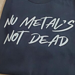 May include: A dark blue t-shirt with the white text "Nu Metal's Not Dead" printed on the front.