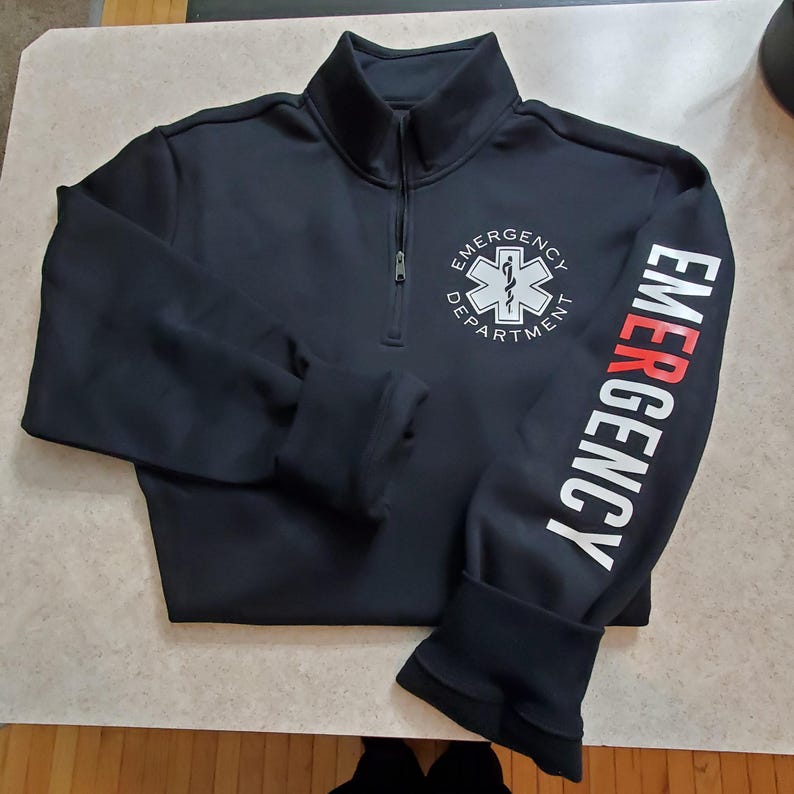 May include: Black quarter-zip pullover sweatshirt with a white embroidered star of life and the text "Emergency Department" on the front. The right sleeve has the word "Emergency" in white with a red "E".
