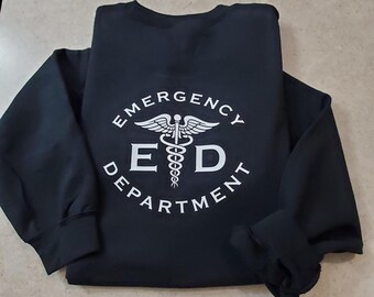 May include: Black sweatshirt with the words "EMERGENCY DEPARTMENT" in a circular design, with a medical symbol in the center. A black and white skull and crossbones design is visible in the upper left corner.
