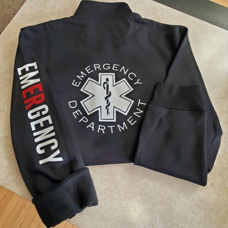 May include: Black zippered sweatshirt with the words "Emergency Department" printed on the back and the word "Emergency" printed on the left sleeve. The back features a white star of life symbol with a snake and staff.