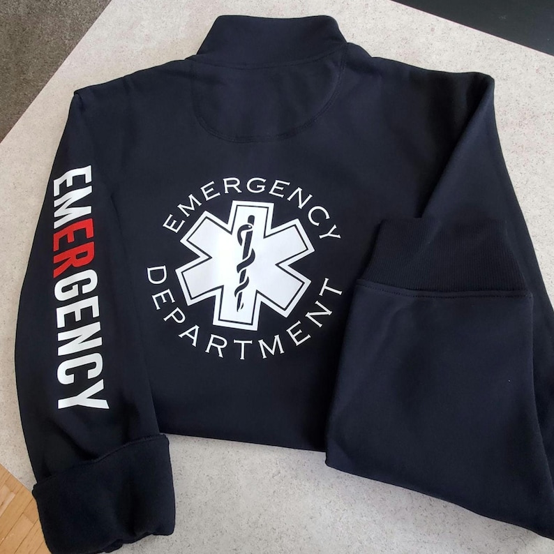 May include: Black zippered jacket with a white star of life logo and the text "Emergency Department" on the back. The left sleeve has the word "Emergency" printed vertically in white with a red stripe.