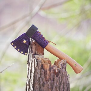 May include: A small purple leather-wrapped axe with a wooden handle, resting on a tree stump. The axe has a leather sheath with brass rivets.