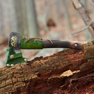 May include: A small green leather axe sheath with a brown leather handle and a black metal axe head. The axe head has the text "PRANDI ITALY" on it.