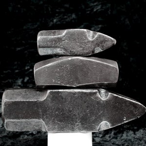 May include: Three stacked metal hammers with a black background. The top hammer has a pointed end, the middle hammer has a rounded end, and the bottom hammer has a pointed end.