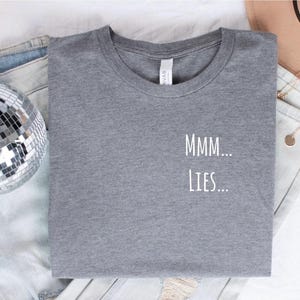 May include: Gray t-shirt with the text "MMM... LIES..." printed in white.
