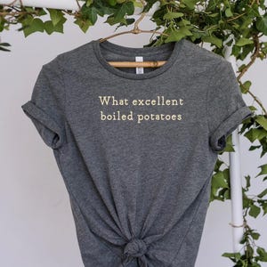 May include: A dark gray t-shirt with the text "What excellent boiled potatoes" printed in white on the front.