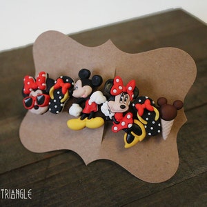 May include: A set of four Disney character hair clips featuring Mickey Mouse and Minnie Mouse. The clips are made of plastic and have a black and white polka dot pattern. The clips are red, black, white, and yellow.