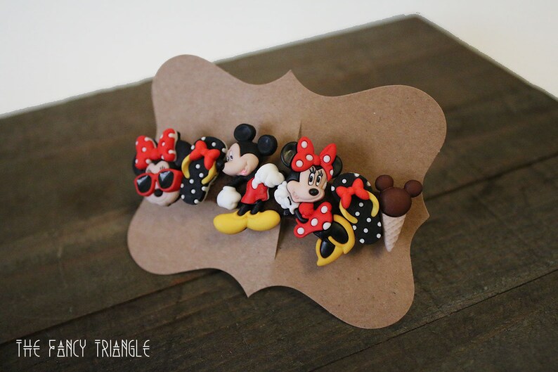 May include: A set of four Disney character hair clips featuring Mickey Mouse and Minnie Mouse. The clips are made of plastic and have a black and white polka dot pattern. The clips are red, black, white, and yellow.