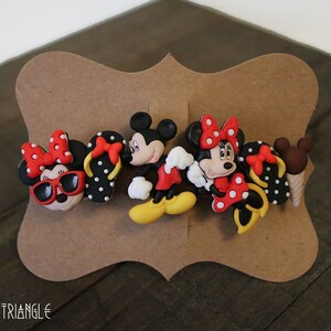 May include: Set of four colorful hair clips featuring Mickey Mouse and Minnie Mouse characters. The clips are made of plastic and have a black and white polka dot pattern. The characters are wearing red and white outfits and have black eyes and noses.