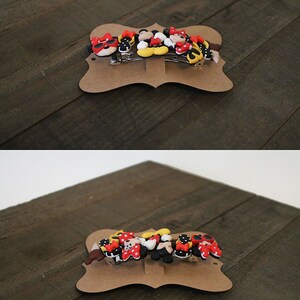 May include: A set of six colorful hair clips featuring Mickey Mouse and Minnie Mouse characters. The clips are made of plastic and have a variety of designs, including Mickey Mouse with sunglasses, Minnie Mouse with a bow, and a Mickey Mouse head. The clips are displayed on a brown card with the text "THE FANCY TRIANGLE".