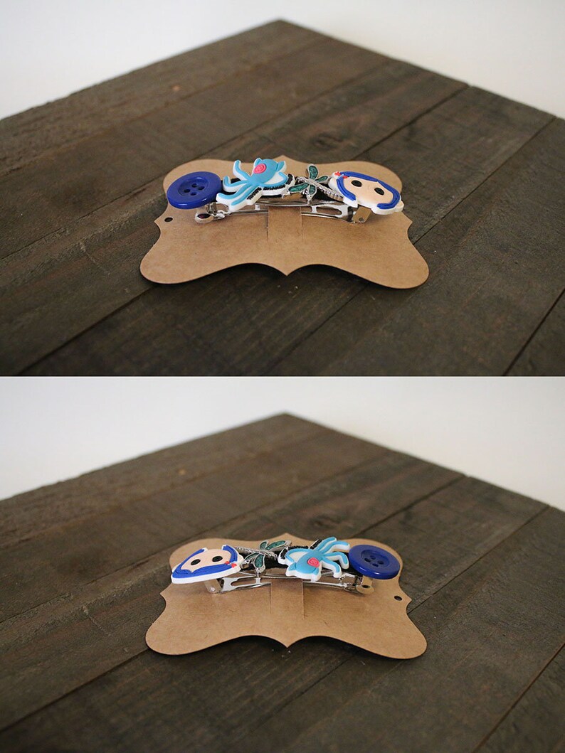 Puede incluir: Dos horquillas decorativas sobre una tarjeta marr&oacute;n. Una presenta un bot&oacute;n azul, una flor azul y un personaje de dibujos animados. La otra tiene un pulpo azul y un personaje de dibujos animados. Las horquillas son plateadas.