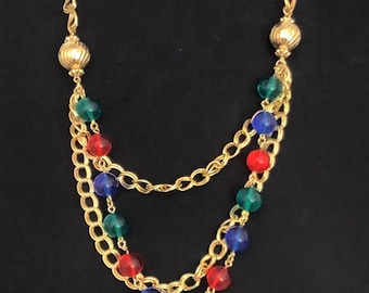 May include: A gold chain necklace with multiple strands and colorful glass beads. The beads are red, blue, and green.