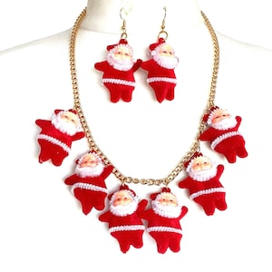 May include: A gold chain necklace with seven red felt Santa Claus ornaments. The necklace is paired with matching earrings, each featuring a red felt Santa Claus ornament.