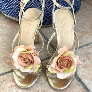May include: Gold high-heeled sandals with a floral embellishment on each strap. The sandals are made by Office London.