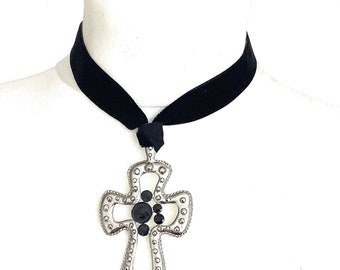 May include: A black velvet choker necklace with a silver cross pendant featuring black gemstones.