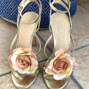 May include: Gold heeled sandals with a large pink flower embellishment on each strap. The sandals are labeled "Office London".