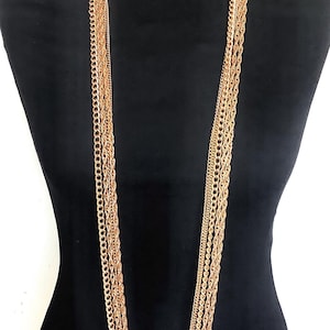 Może przedstawiać: Złoty naszyjnik z wieloma warstwami łańcuchów w różnych stylach. Naszyjnik jest długi i sięga do klatki piersiowej.