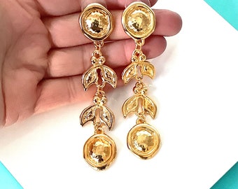 May include: A pair of gold dangle earrings with a hammered disc design and three leaf-shaped charms hanging from each disc.